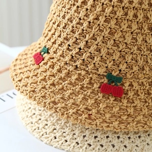 Close-up of handmade straw sun hat featuring detailed red cherry embroidery and tight weave