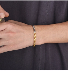 Detail of two-tone gold and silver Miami Cuban link bracelet worn on wrist over knitwear