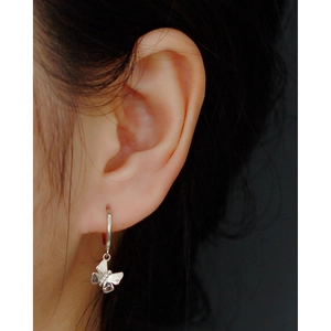 Close-up of a silver butterfly pendant hoop earring worn on a model ear lobe