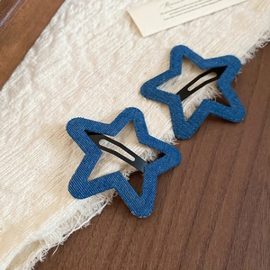Detail of two star-shaped blue denim hair clips on a textured rustic background