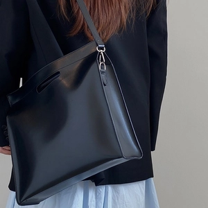 Minimalist black leather tote bag for laptops shown being carried by a model