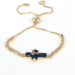 Detailed macro view of gold-plated cross bracelet with blue zircons and slider clasp