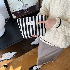 Detail of a large canvas striped makeup bag held by a model in a retro setting