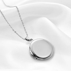 Polished silver stainless steel round locket necklace on white silk background