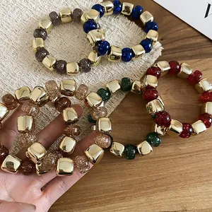 Colorful acrylic bead stretch bracelet with gold cube metal accents on wood background