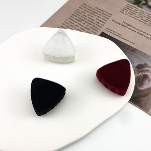 Three elegant flocked triangular hair clips in white, black, and burgundy on a ceramic tray