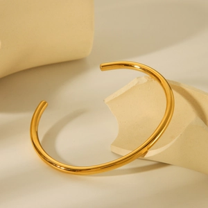 Minimalist 18K gold-plated stainless steel open bangle on a geometric background