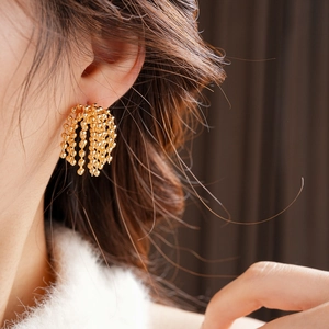 Detail of gold-plated fringe tassel earrings with metal beads on a model's ear