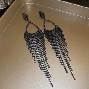 Detailed view of long black rhinestone tassel earrings on a champagne metal tray