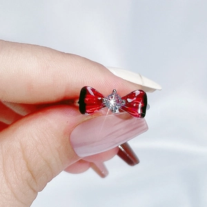 Macro detail of silver-tone ring featuring a red butterfly bow with a sparkling center stone