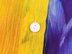 Macro shot of yellow and blue floral chiffon fabric with a white button detail