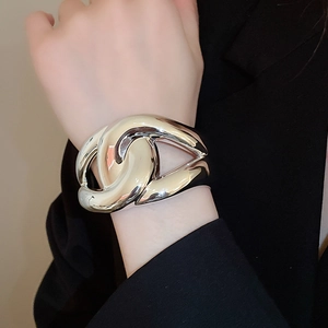Close-up of wide silver metal cuff bracelet featuring a bold interlocking double C design