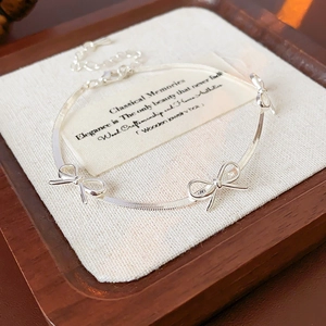 Silver bow snake chain bracelet displayed on a premium dark wood jewelry tray