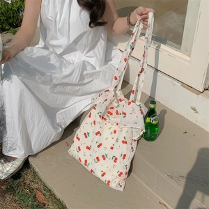 Detail of canvas tote bag featuring cherry print and ruffled trim in outdoor setting
