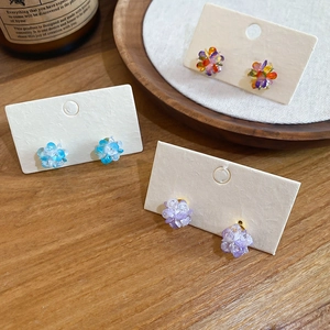 Close-up of elegant floral cluster stud earrings in blue and purple on a wooden display