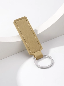 Close-up of beige PU leather keychain with silver metal ring on white geometric stand