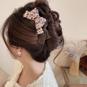 Elegant woman wearing large brown acrylic hair claw with tweed bow in cozy home setting