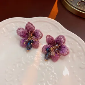Elegant purple fabric flower earrings with crystal beads on a white vintage ceramic plate