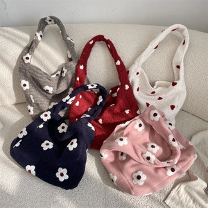 Detailed pile of five plush tote bags with daisy flowers on a textured white sofa