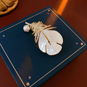 Macro shot of gold-plated feather brooch with zircon pave and mother of pearl inlay