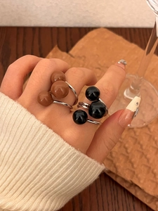 Detail of silver rings with brown and black ball accents worn by a model in soft lighting