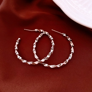 Macro shot of silver metal hoop earrings with diamond-cut texture on red silk fabric