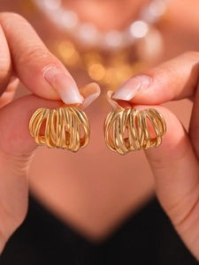 Macro shot of gold ribbed C-shaped stud earrings featuring layered winding lines