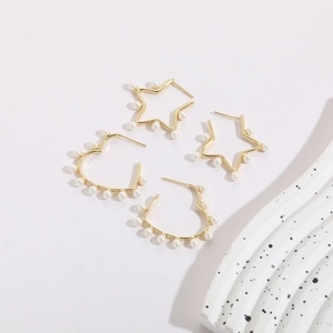 Detail of star and heart gold-plated earrings with pearls on a soft purple background