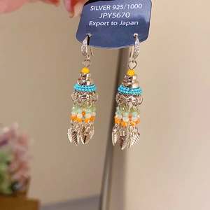Detail of colorful beaded tassel earrings with silver leaves on brand display tag