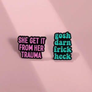 Detail of two enamel pins with funny phrases on a minimalist pink background