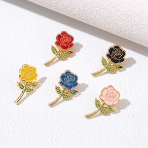 Detail of five colorful enamel rose brooches with golden metal edges and green leaves