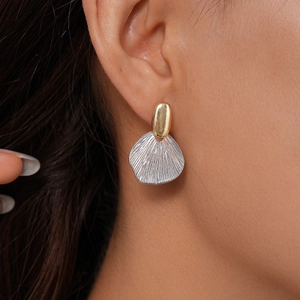 Detailed view of model wearing gold and silver geometric fan-shaped earrings with textures