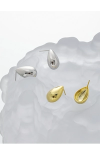 Detailed close-up of polished silver and gold teardrop earrings on frosted glass base