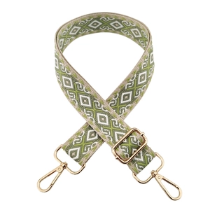 Close-up of green and beige ethnic geometric patterned wide bag strap with gold buckles