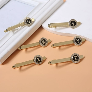 Close-up of golden letter tie clips with black enamel and sparkling diamond borders