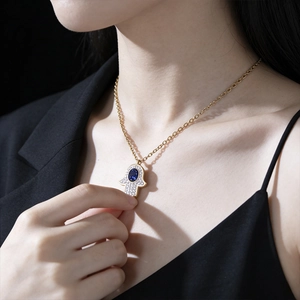 Gold Hamsa Hand pendant necklace with crystals and blue stone worn by a model