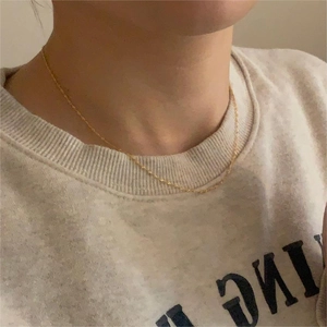 Close-up of minimalist gold water wave chain necklace worn by a model in soft light
