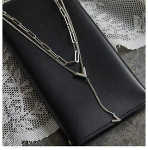 Detail of silver double-layered V-pendant necklace on black leather background