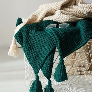 Detailed view of dark green and beige knitted blankets with tassels in a storage basket