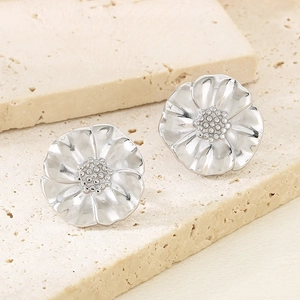 Macro shot of silver floral earrings with petal textures on beige textured stone
