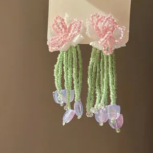 Detailed macro of floral beaded tassel earrings with green beads and purple tulip charms