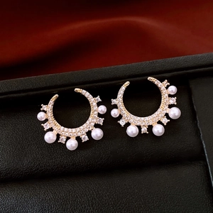 Macro shot of gold-plated C-shape earrings with inlaid zircons and pearls on black leather
