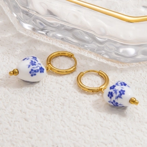 Detail of heart-shaped blue and white ceramic earrings with 18k gold-plated hoops