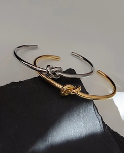 Detail of gold and silver knot bangles displayed on black rock with light and shadow
