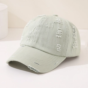 Detailed view of the light green washed cotton fabric and distressed holes on the baseball cap