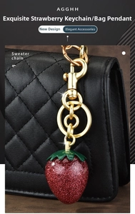 Detailed close-up of a red glitter strawberry keychain with gold hardware on a black bag