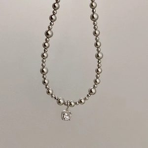 Macro detail of a square zircon pendant and gradient grey pearl necklace on a clean background