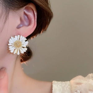 Detailed close-up of a raffia daisy earring with white petals and golden center on a model