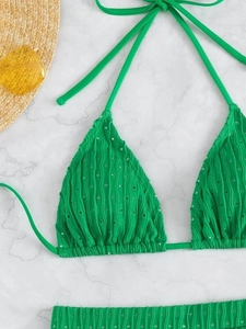 Flat lay of green bikini with wavy texture, eyelet details, and beach accessories
