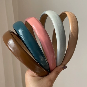 Five assorted glossy leather-like headbands in multi-color held against a plain wall
